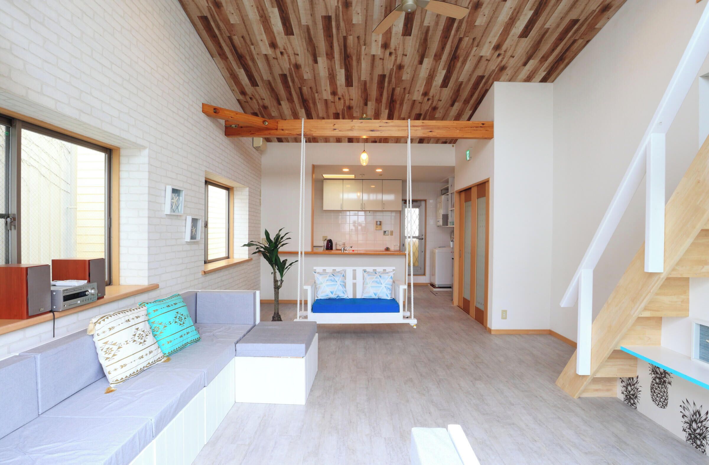 A modern interior with a wooden ceiling, a swing, a sofa with cushions, a small plant, and a staircase.