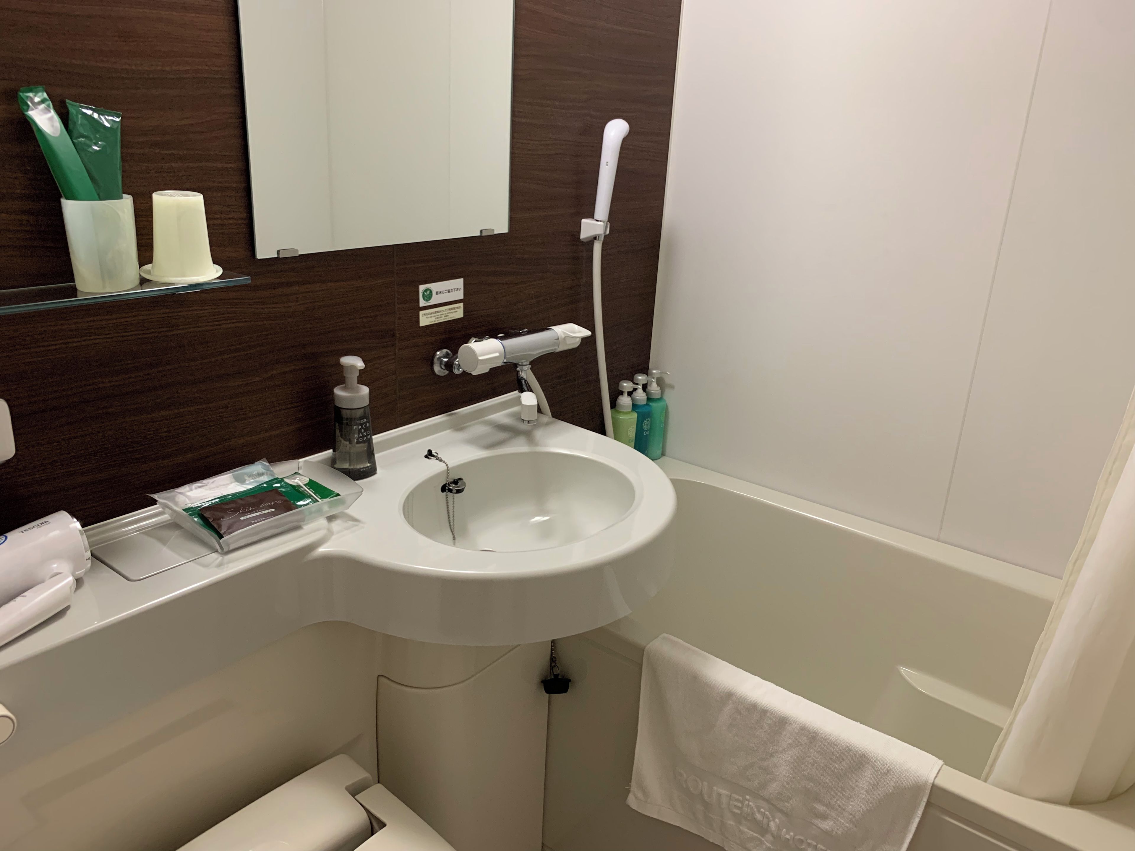 A bathroom with a white sink, a mirror, a towel hanging on the wall, and toiletries on the counter.