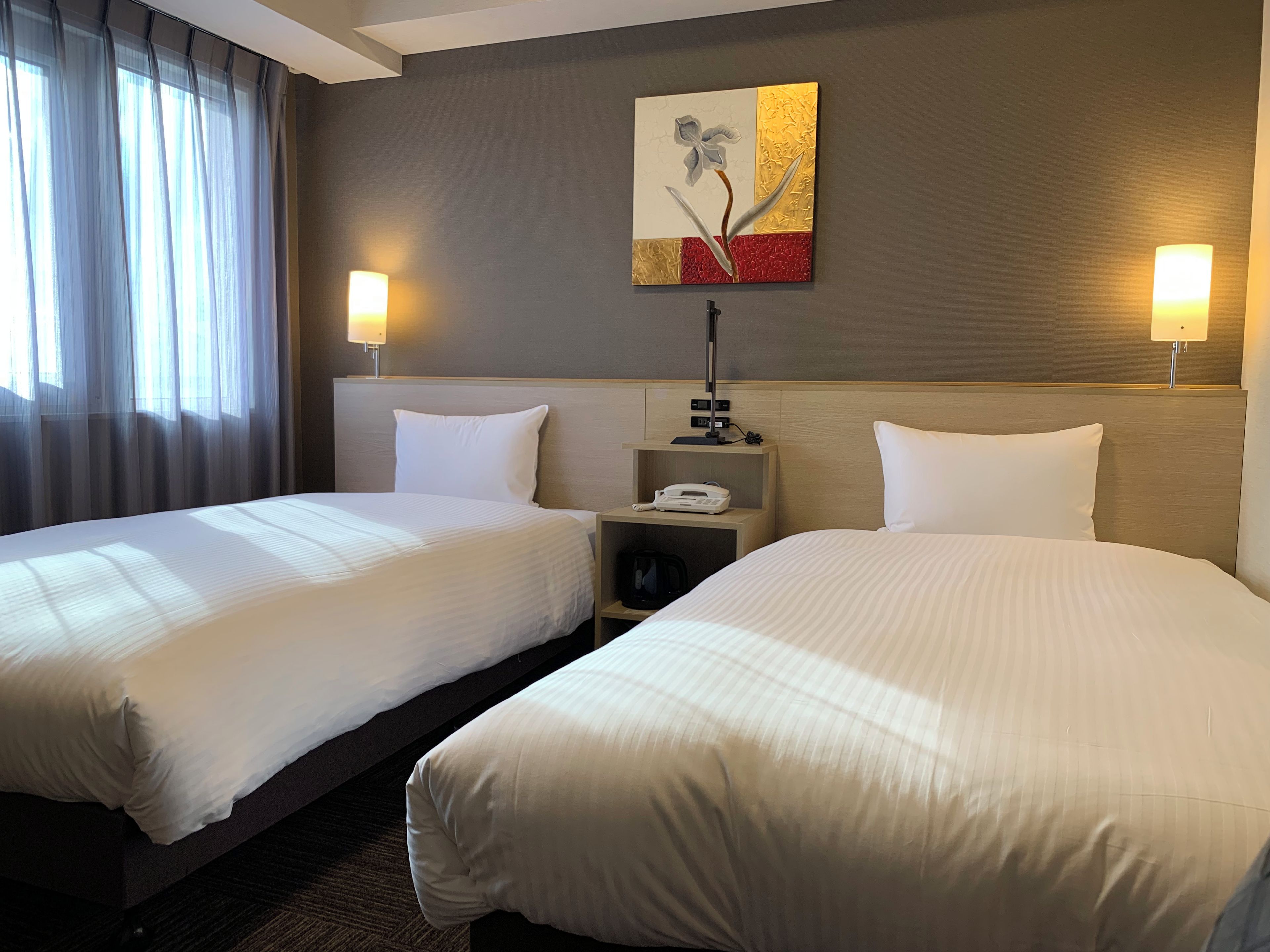 A hotel room with two beds, a nightstand with a lamp, and a painting on the wall.