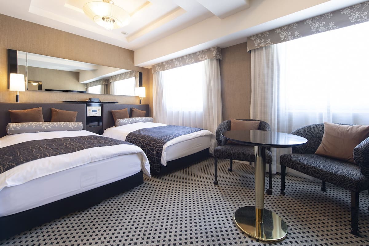A hotel room with two beds, a desk, and a chair.