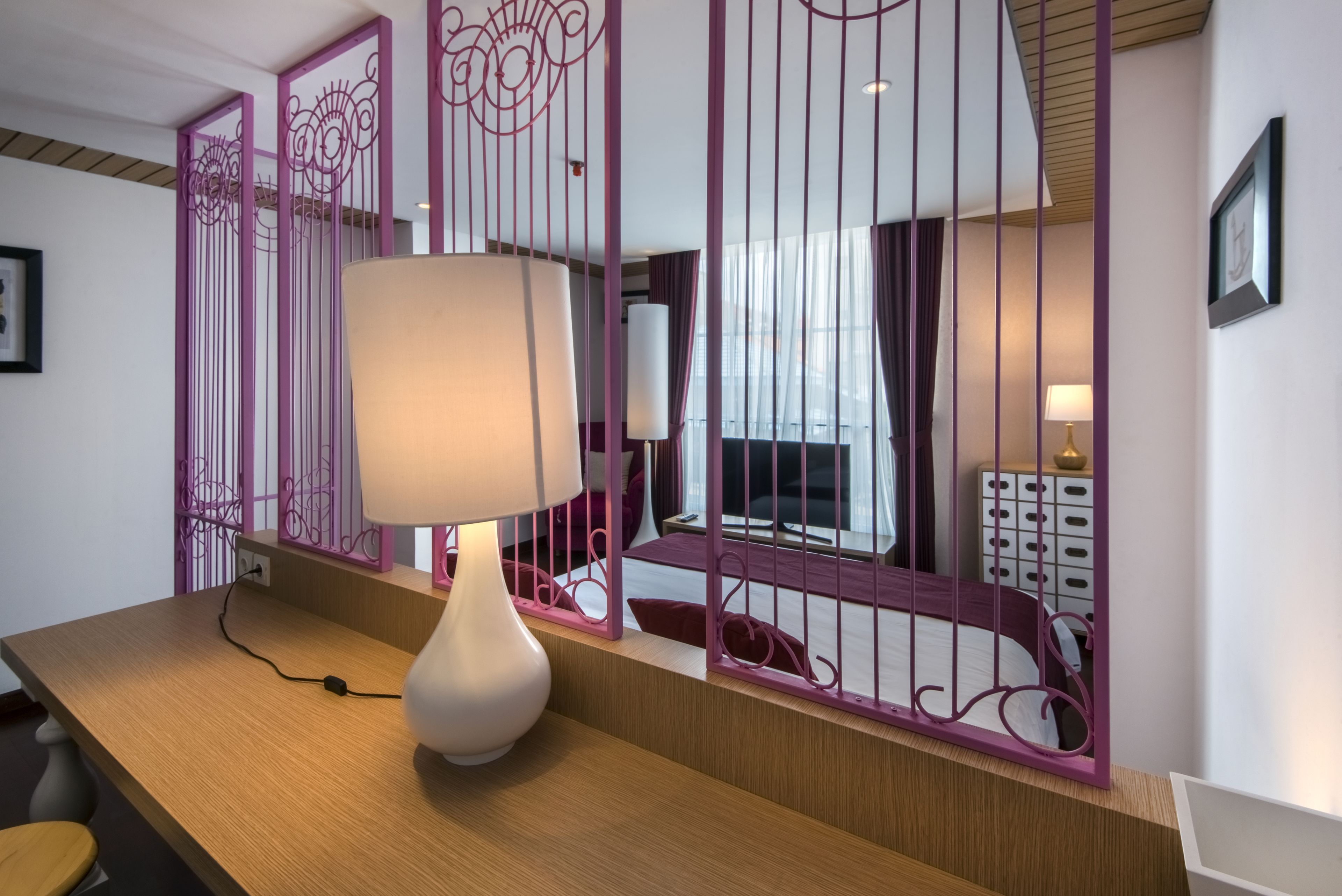 A room with a wooden desk, a white lamp, and a purple decorative partition.