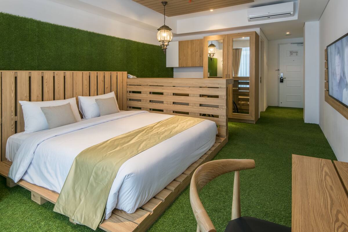 A bedroom with a wooden bed, green artificial grass, a wooden chair, and a small table.