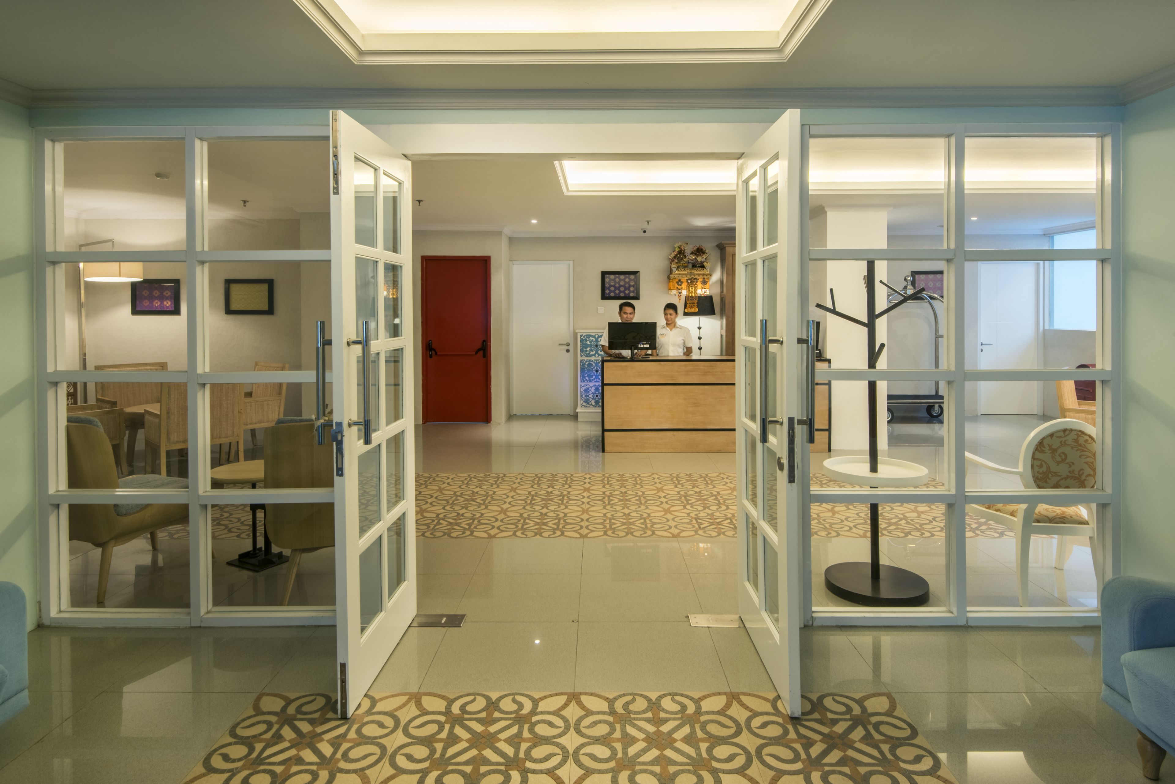 A hotel lobby with open glass doors leading to a reception area and a dining area.
