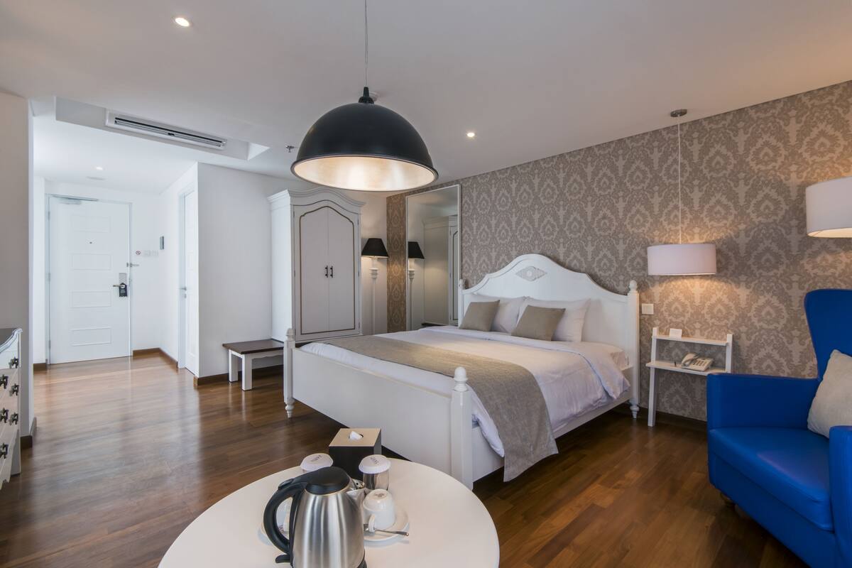A modern bedroom with a large bed, bedside tables, a blue armchair, and a round coffee table.