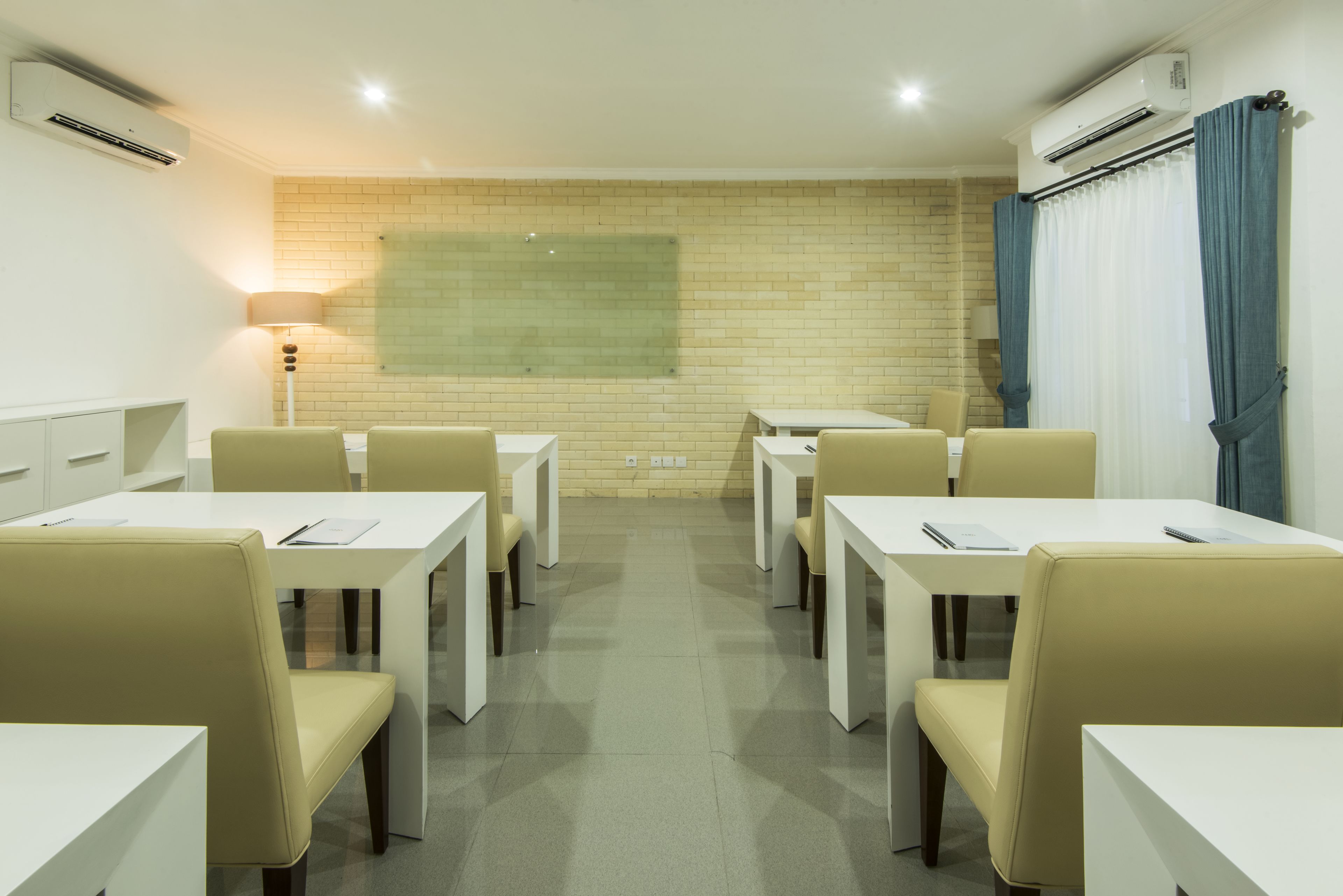 Uma sala de conferências com mesas e cadeiras brancas, parede de tijolos e tela de projeção.