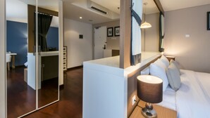 Una camera d'albergo moderna con uno specchio grande, un comodino in legno con una lampada, un divano e vista sul corridoio.