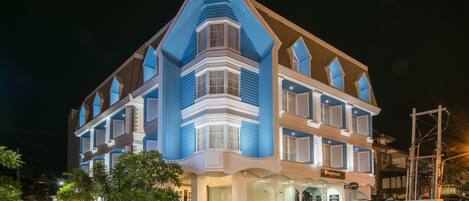 A multi-story hotel with a distinctive blue and white facade, large windows, and a visible entrance with signage.