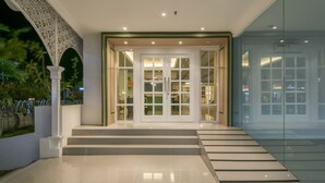 Ingresso moderno di un hotel con facciata in vetro, una scalinata che conduce alle porte e un arco decorativo.