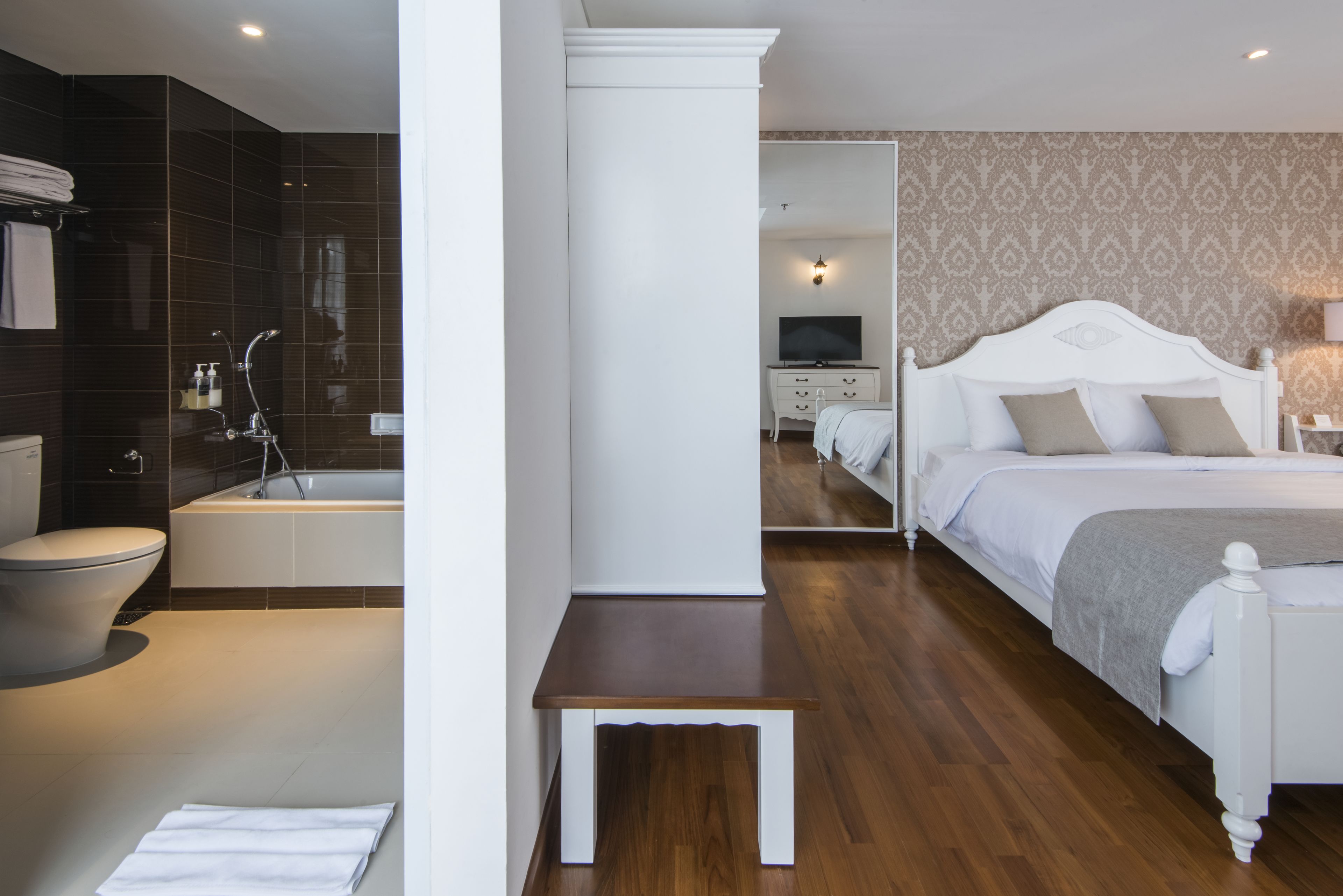 A modern hotel room with a separate bathroom, a bed with white headboard, a bedside table, and a television in the corner.