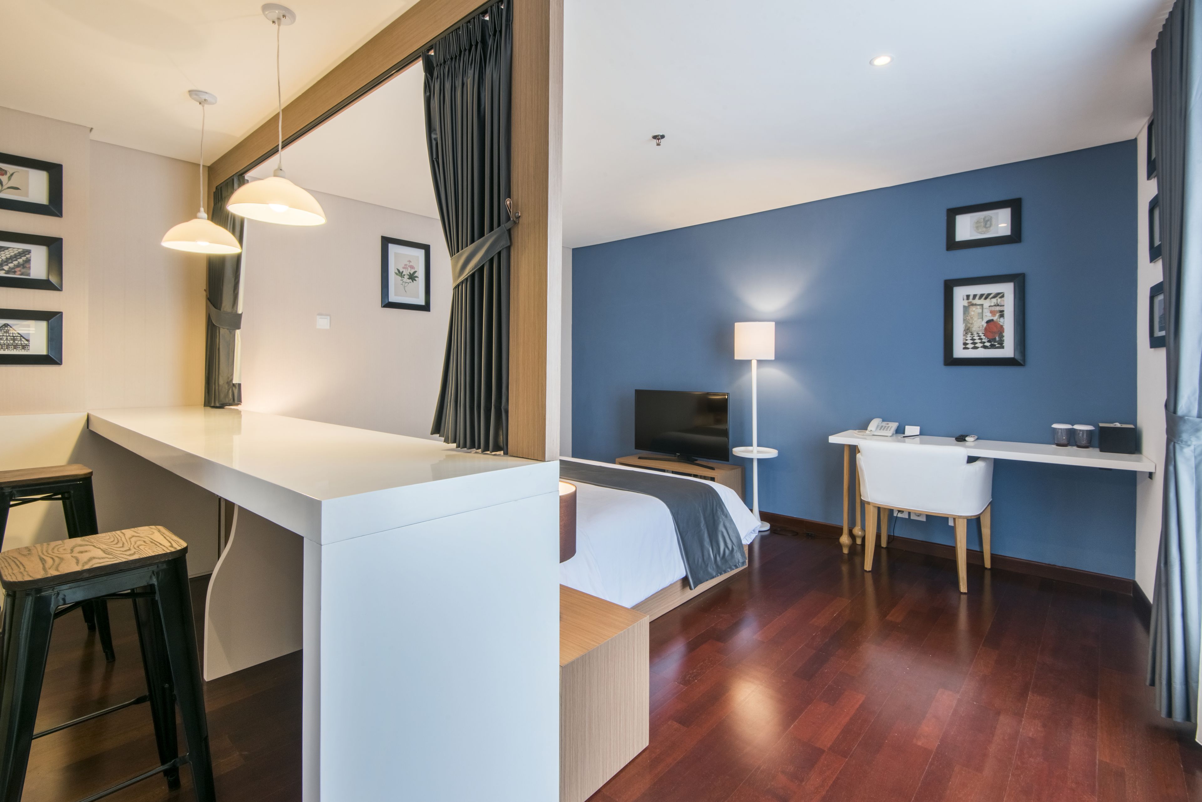 Ein modernes Hotelzimmer mit einem weißen Bett, einem Schreibtisch und einem Fernseher. Es gibt zwei Sessel und eine Lampe.