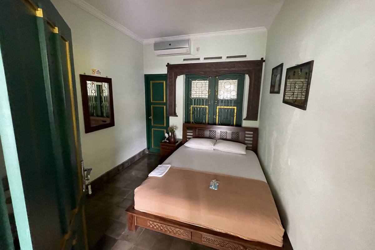 A bedroom with a bed, a wooden headboard, a green door, and a wall-mounted air conditioner.