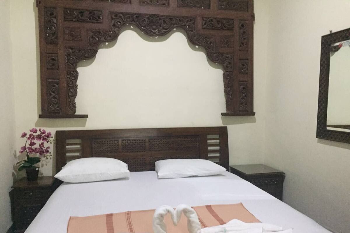 A hotel room with a large bed, a wooden headboard, and a mirror on the wall.