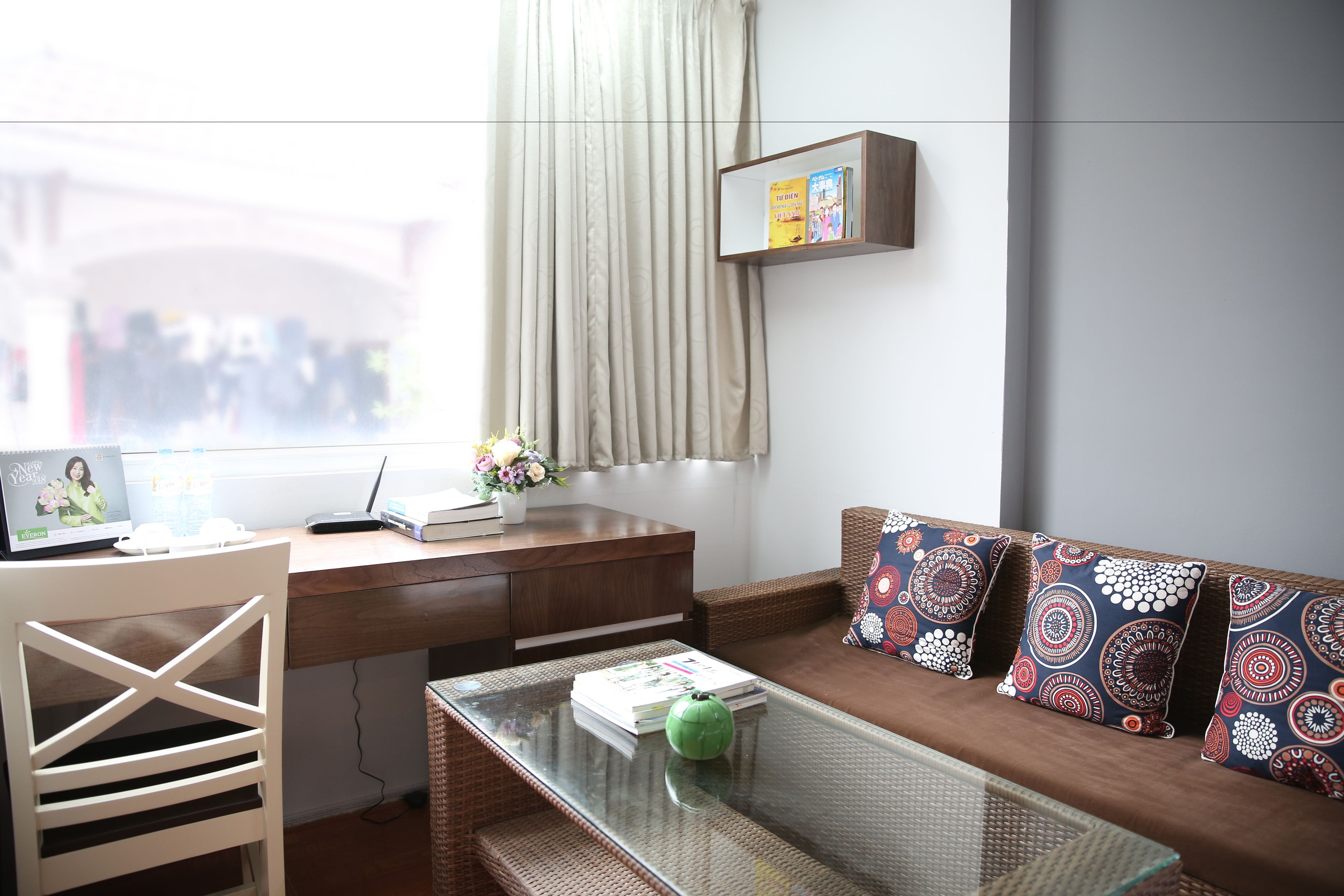 A modern living room with a wooden desk, a glass coffee table, a white chair, and a patterned sofa.