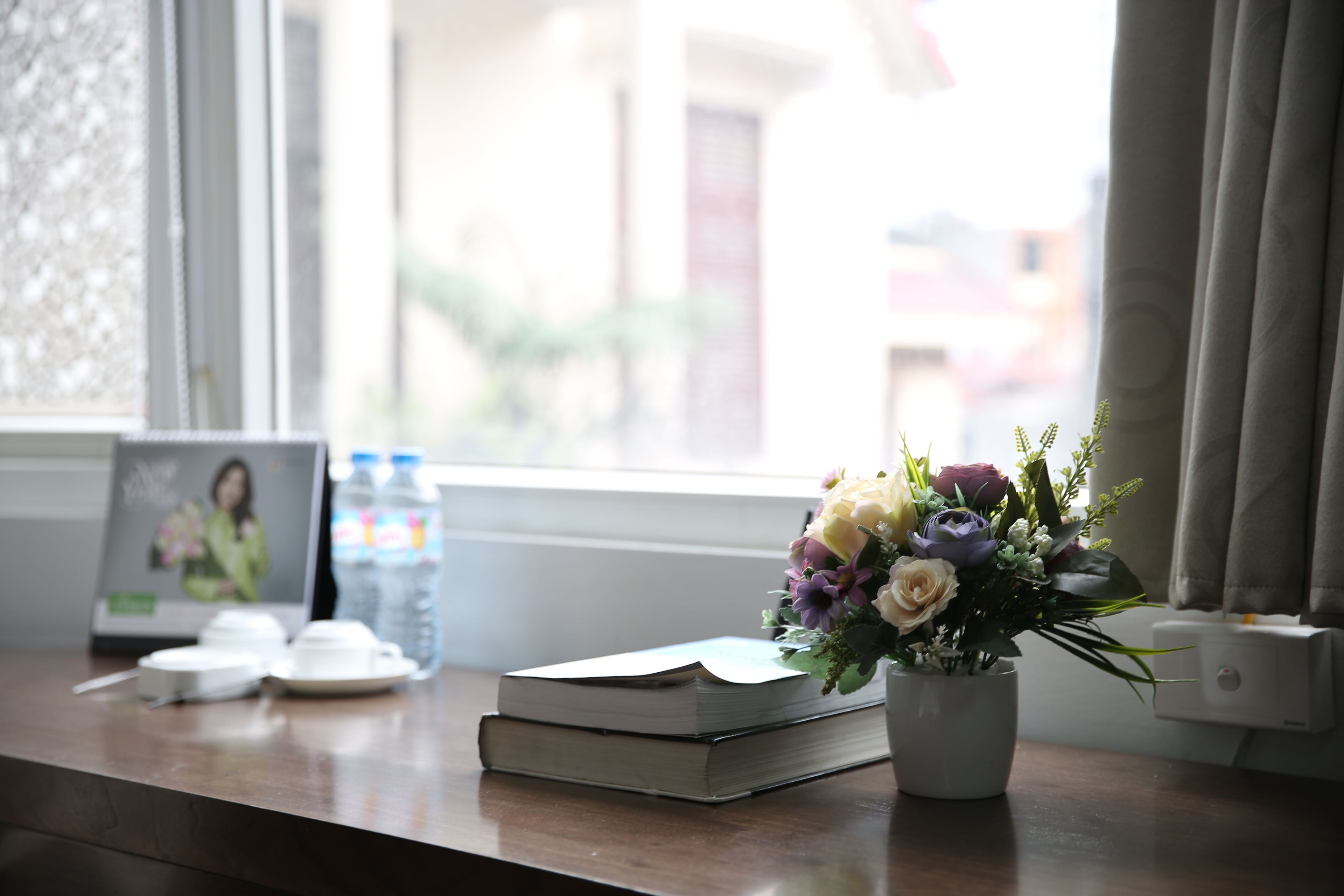 Una mesa de madera con un libro, un florero de flores, una botella de agua y una foto en marco.