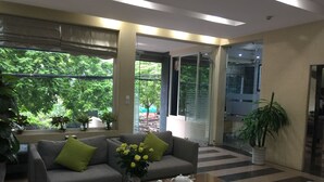A modern lobby with a grey sofa, a coffee table with teapots, and a large window with a view of greenery.