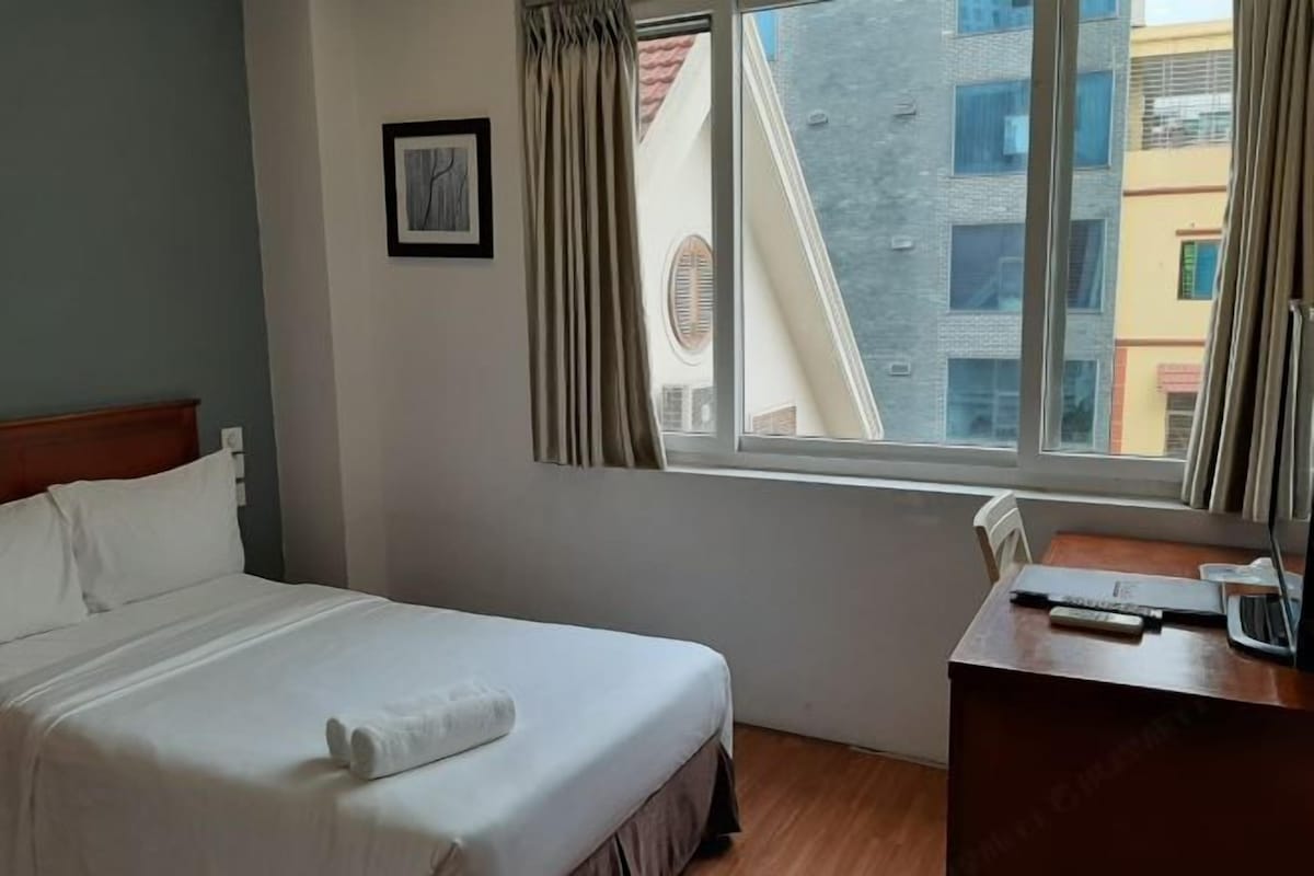 A hotel room with a bed, a desk, a window, and a framed picture on the wall.