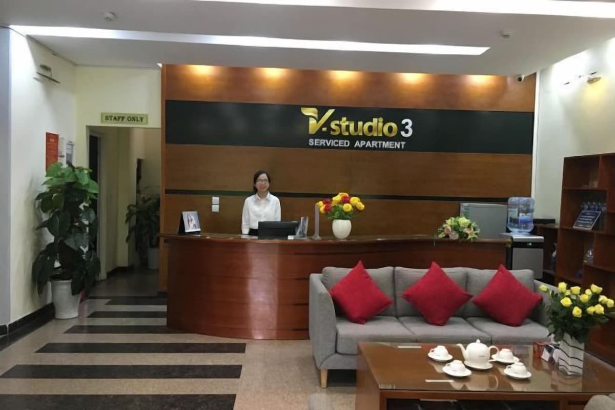 A reception area with a sign reading "Studio 3 Serviced Apartment," a reception desk, a sofa with red cushions, and a table with teapots and cups.