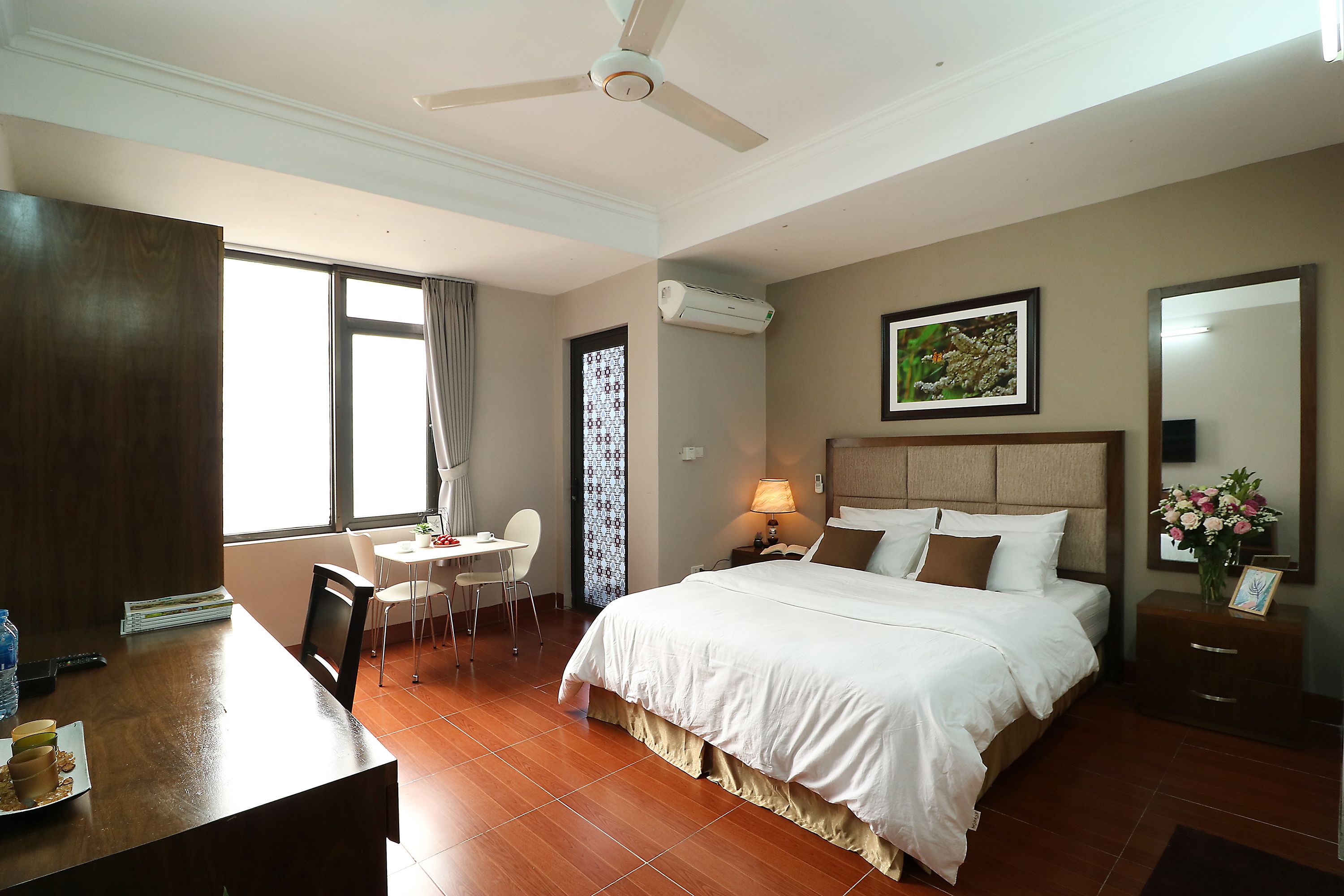 A hotel room with a bed, a desk with a chair, a window, and a ceiling fan.