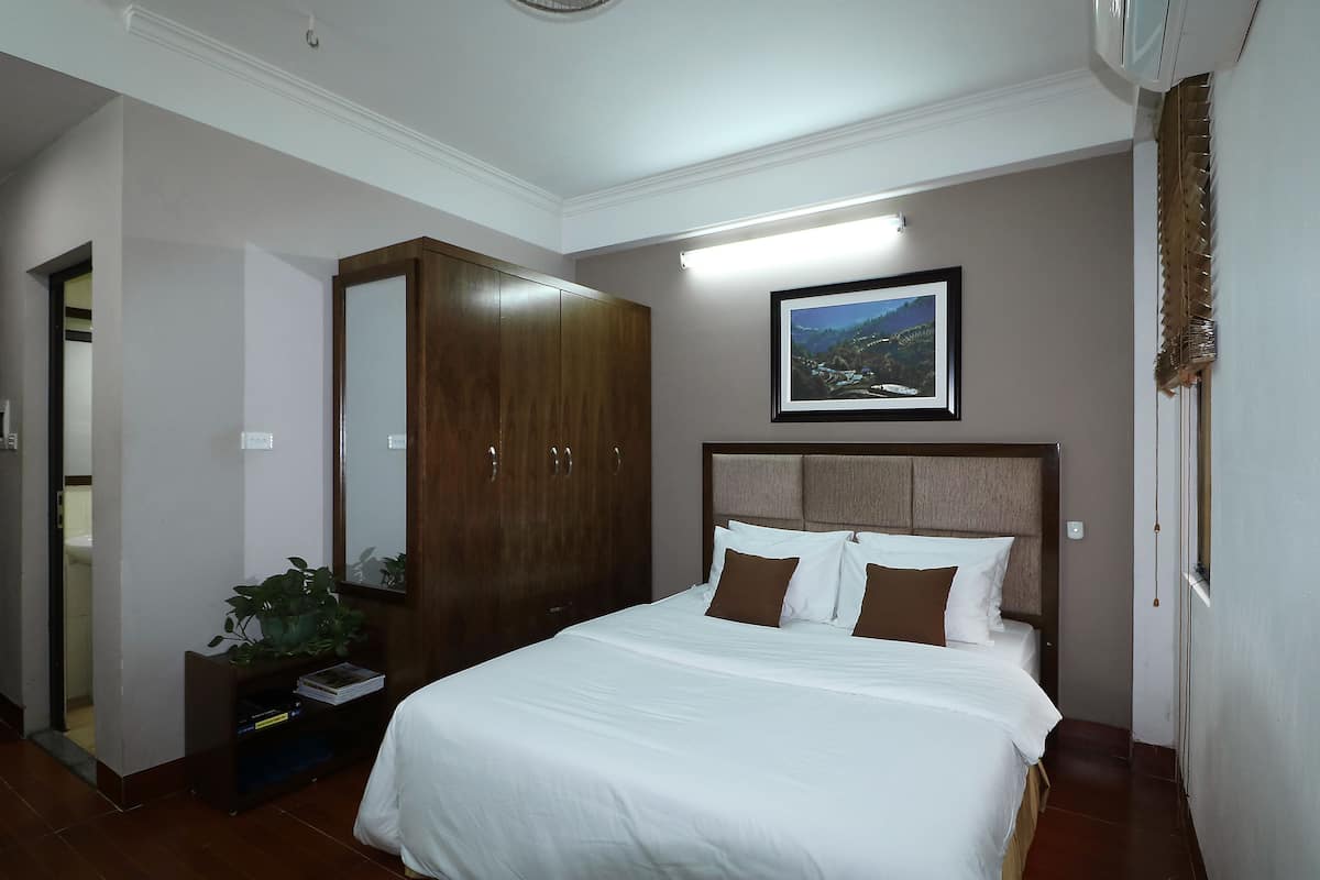 Un dormitorio ordenado con una cama grande, un armario, un cuadro en la pared y una planta pequeña en una mesita de noche.