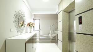 A modern hotel lobby with a white reception desk, a decorative mirror, and a staircase leading to an elevator. - iStay Hotel Apartment 1 (Hanoi)
