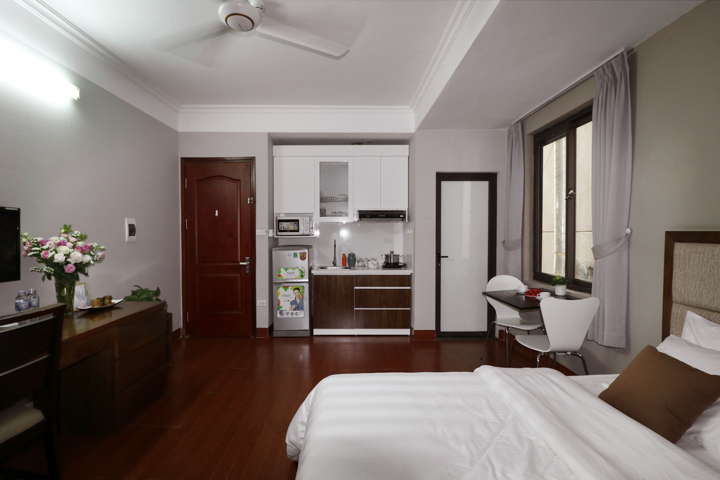 A hotel room with a bed, a desk, a kitchenette, and a TV.