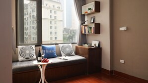 A cozy room with a large window, a built-in bench with cushions, a small table with a bottle and glasses, and a bookshelf against the wall. - iStay Hotel Apartment 1 (Hanoi)
