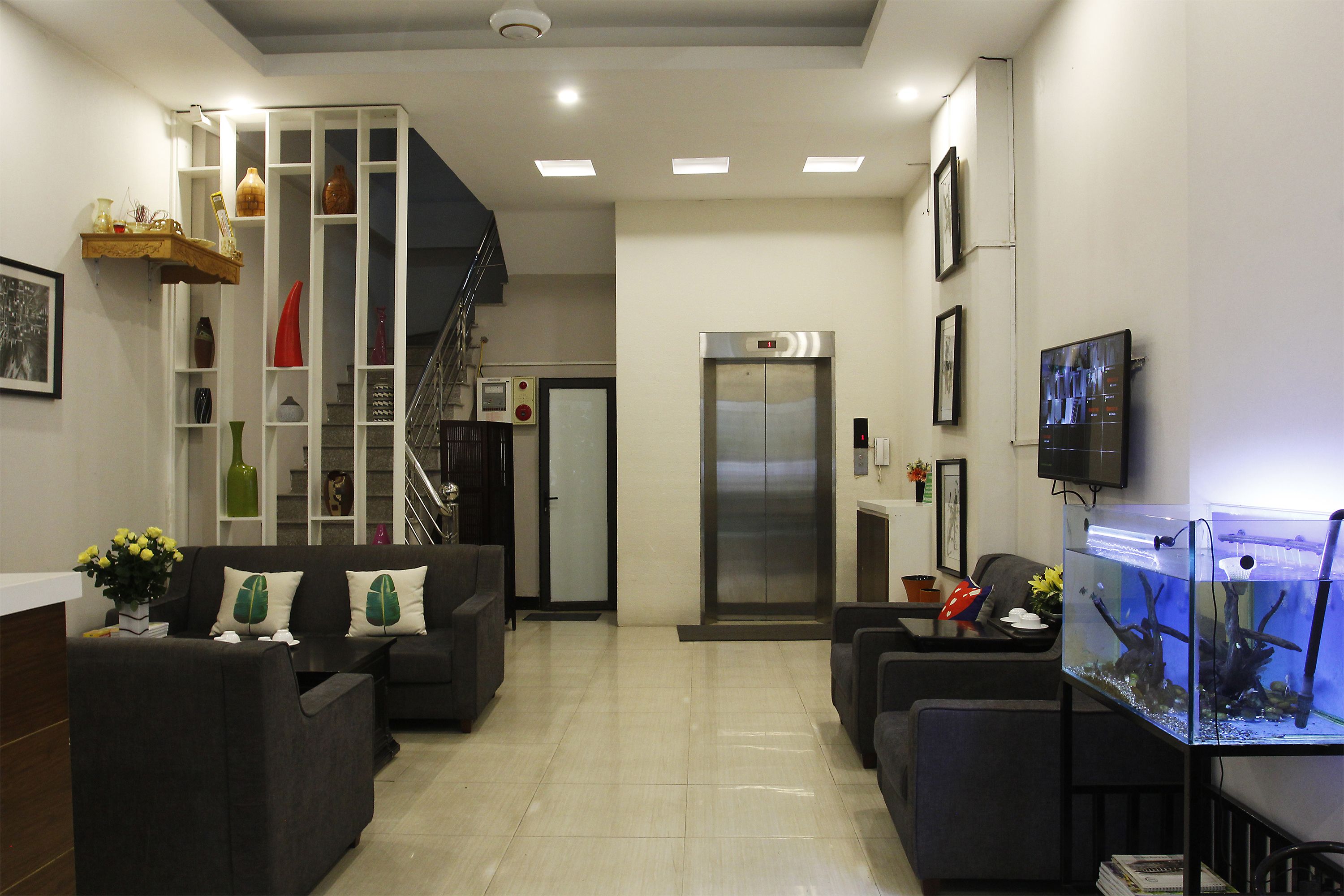 Un vestíbulo moderno con mostrador de recepción, sofás, un acuario y una escalera.