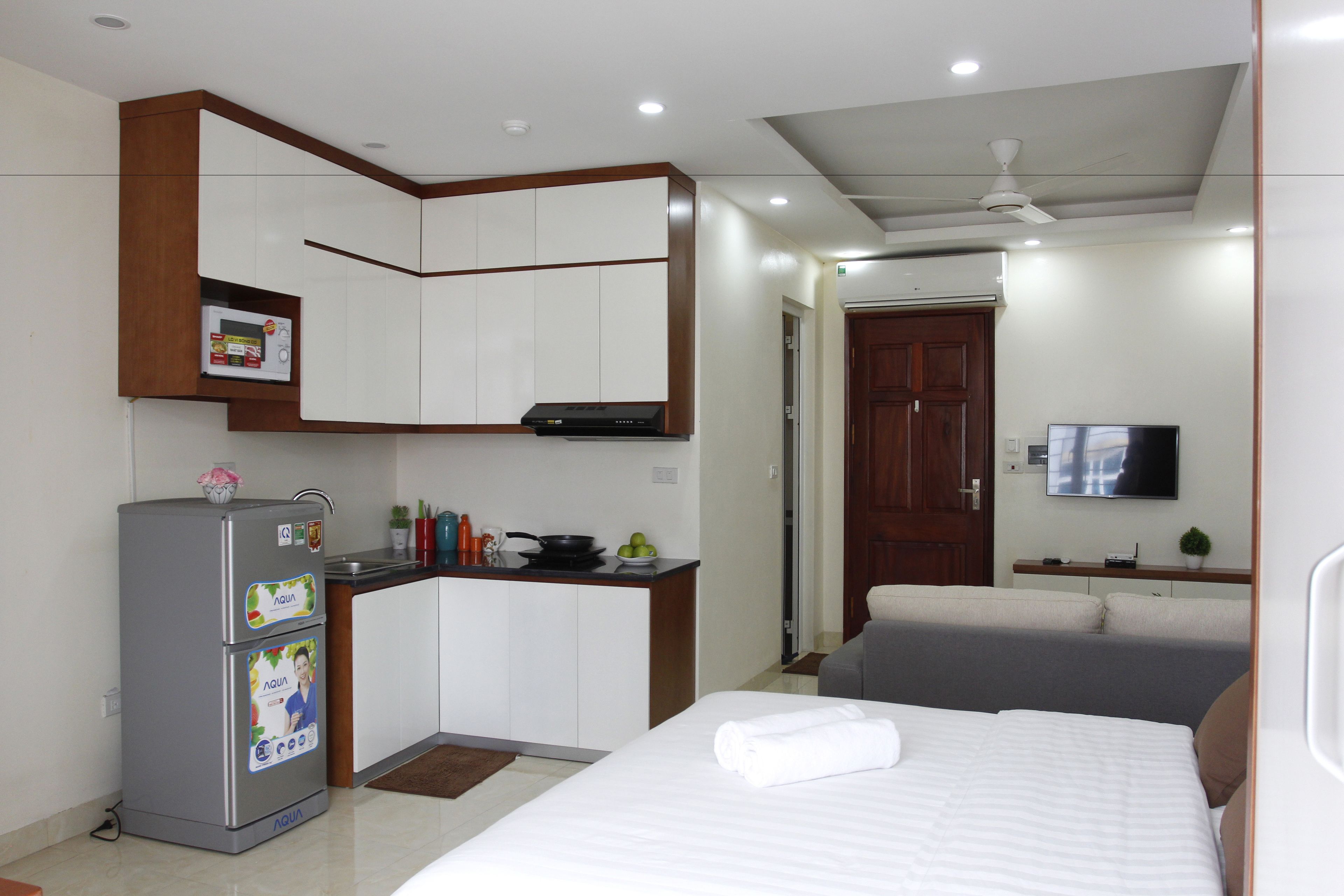 Une chambre d’hôtel de taille réduite, équipée d’une kitchenette, d’un lit, d’une télévision et d’un ventilateur de plafond.