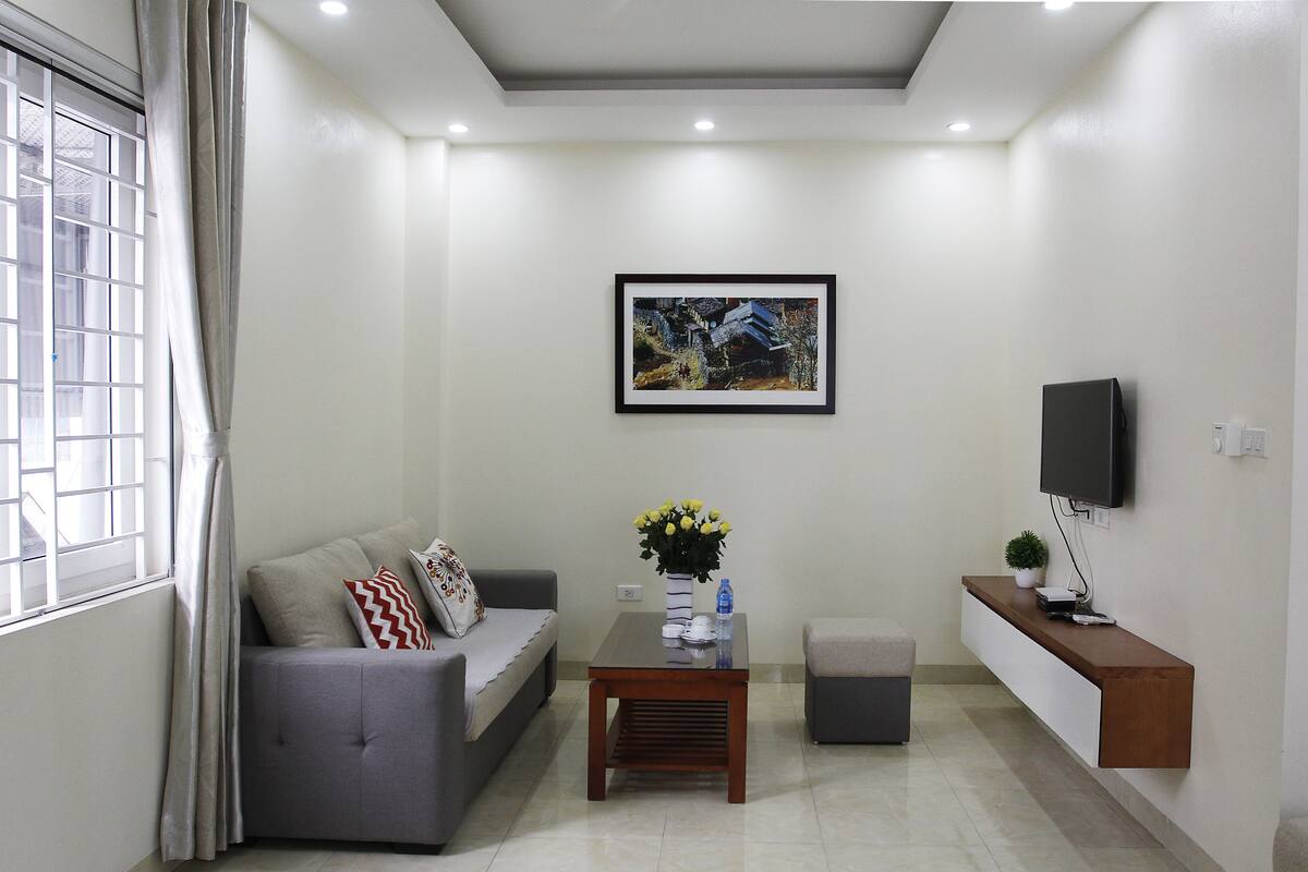 A modern living room with a grey sofa, a coffee table, a small side table, a mounted TV, and a framed picture on the wall.