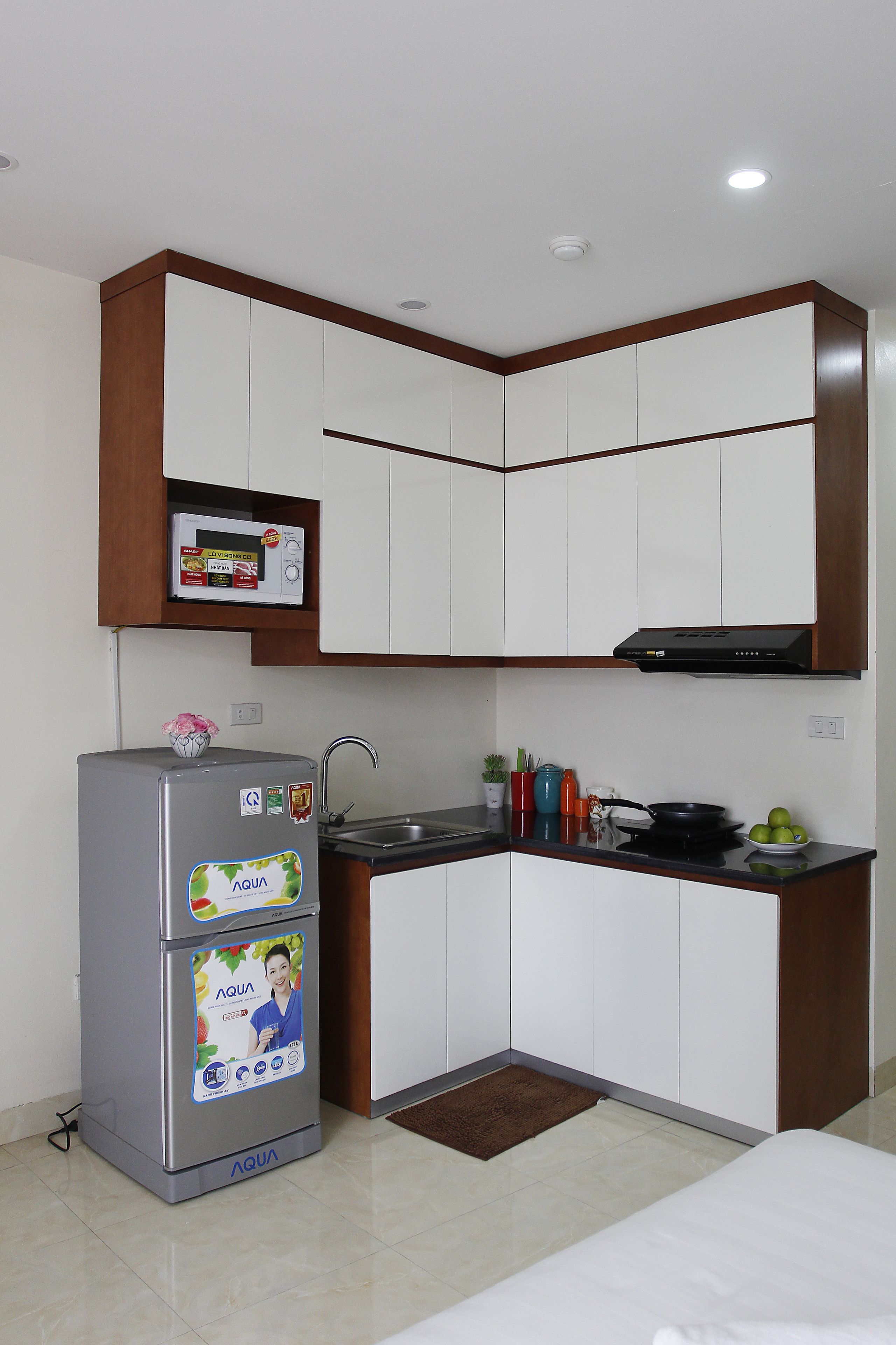 A compact kitchen with white cabinets, a microwave, a refrigerator, and a sink.