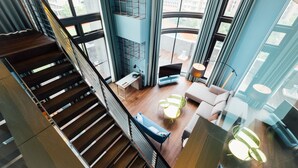 A modern interior with a wooden staircase, a seating area with a sofa and coffee table, and a view of the city through large windows.