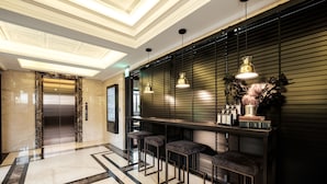 A modern lobby with a marble floor, a reception desk, bar stools, and a decorative wall.