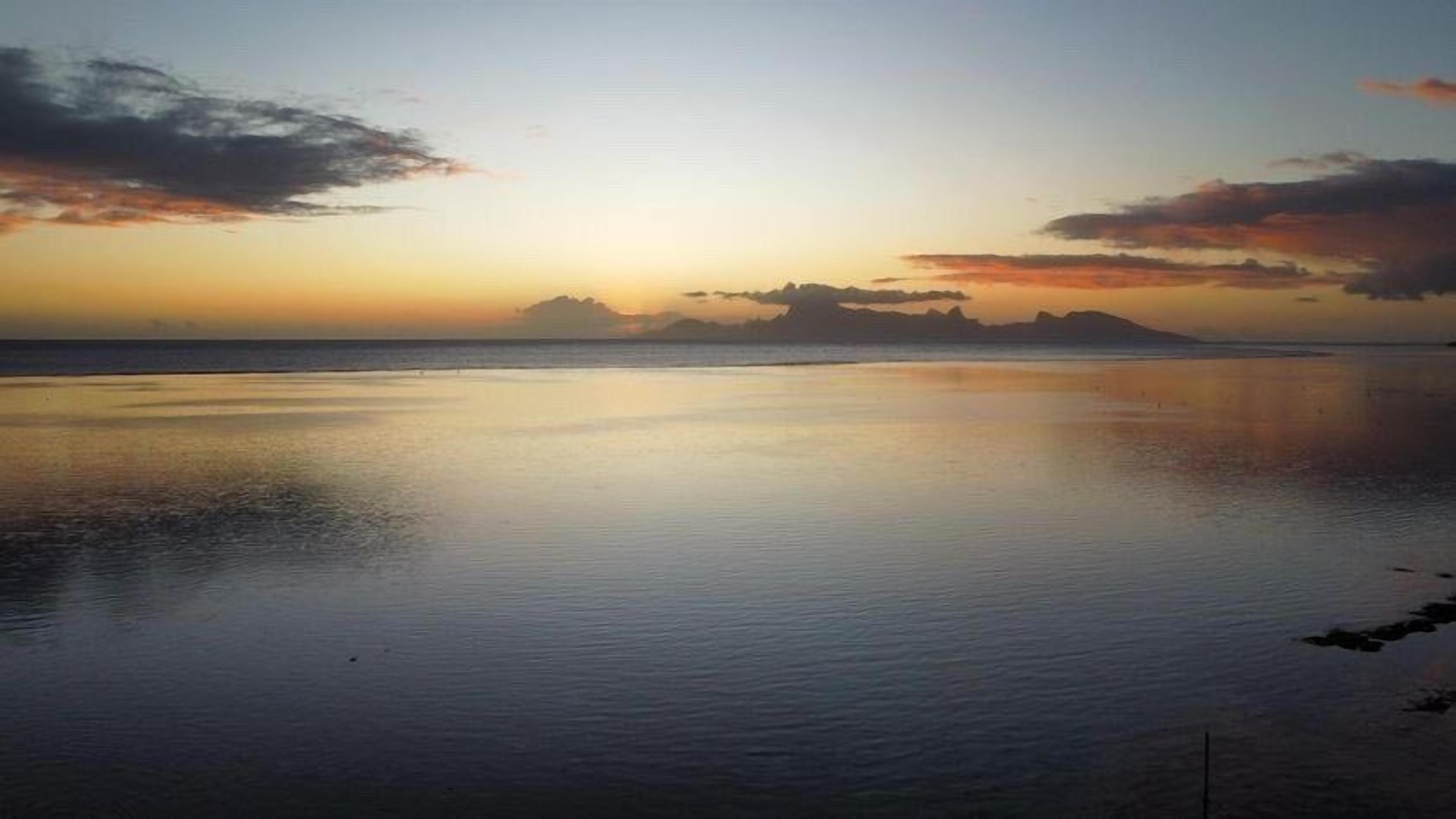 Een rustig strand bij zonsopkomst met een heldere lucht en kalm water dat de hemel weerspiegelt.