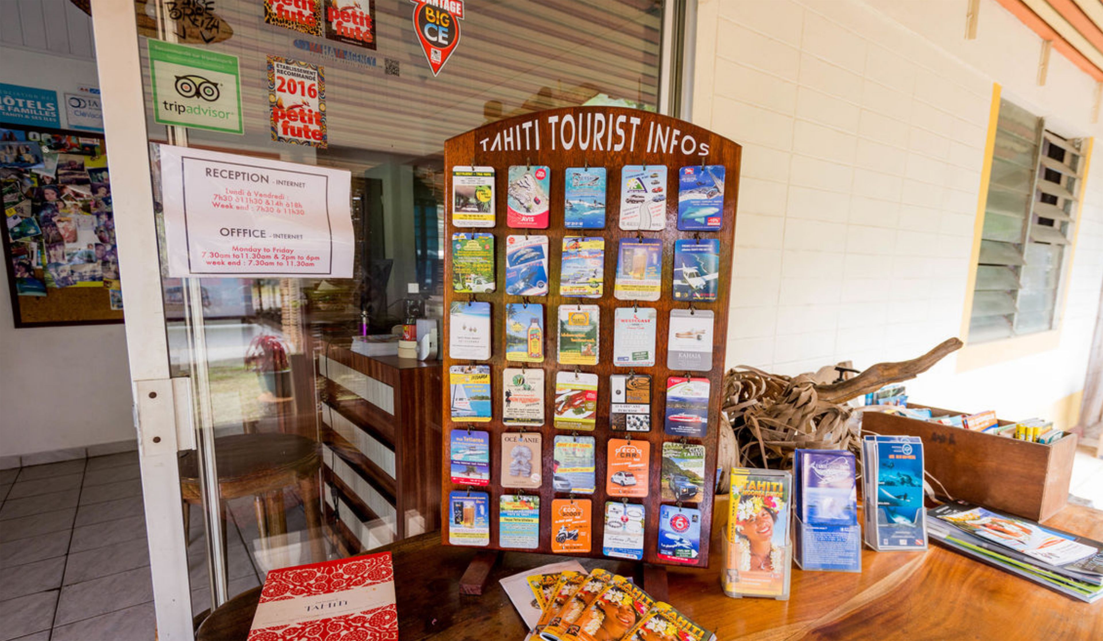 A reception area with a wooden signboard titled "TAHITI TOURIST INFOS" displaying various travel brochures.