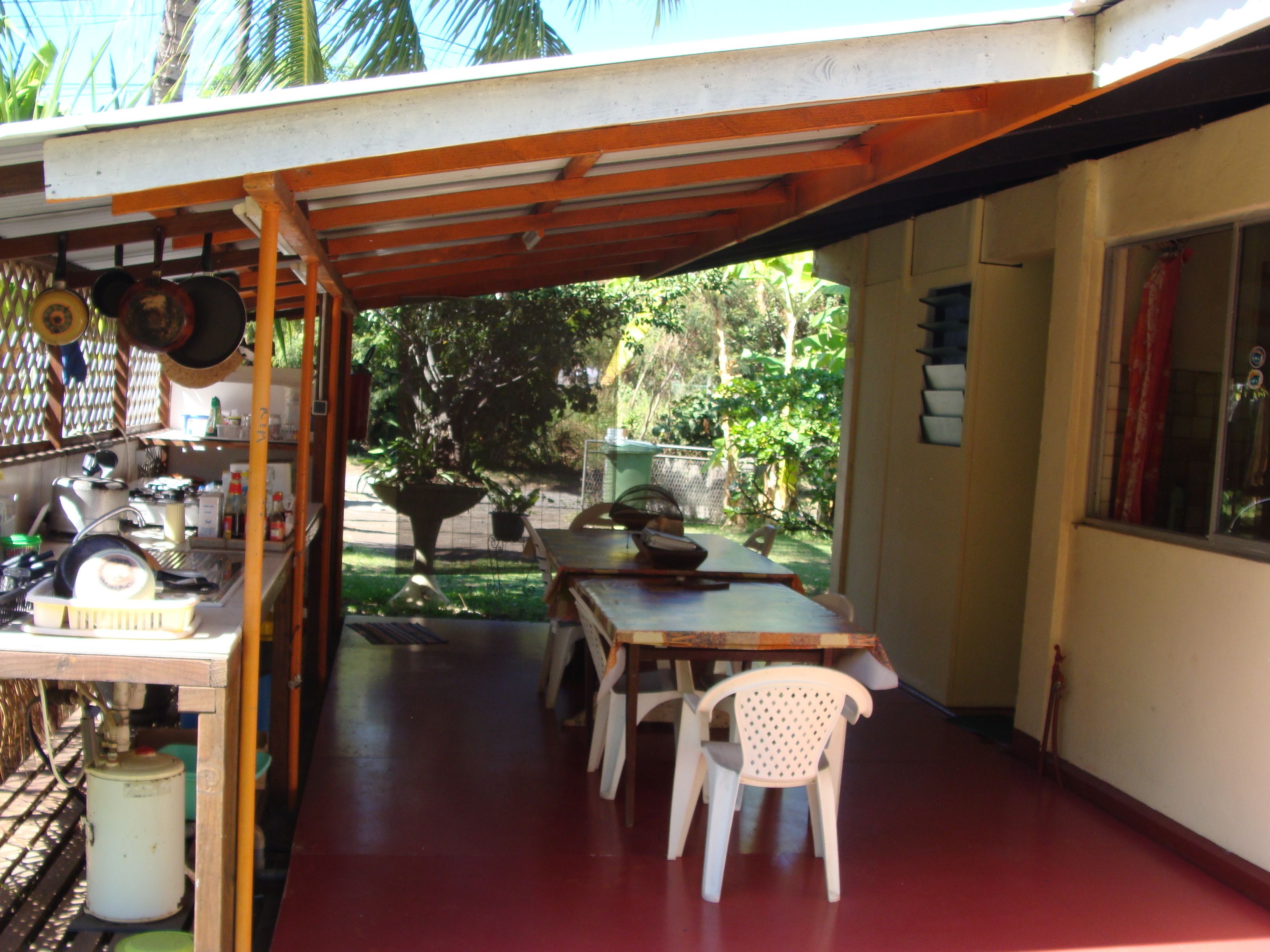Un patio cubierto con una mesa y sillas para comer, un lavamanos y diversos utensilios de cocina.