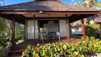 A wooden gazebo with a tiled roof, a covered seating area with a table and chairs, and a view of a lush garden with tropical plants.