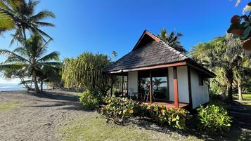 A small, single-story structure with a sloped roof, surrounded by tropical vegetation and palm trees, overlooking a beach.