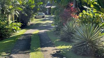 A garden pathway leading to a house with lush greenery and a parked car.