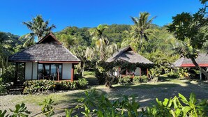 A tropical resort with two thatched-roof huts, surrounded by lush greenery and palm trees. - Punatea Village (Taiarapu-Est)
