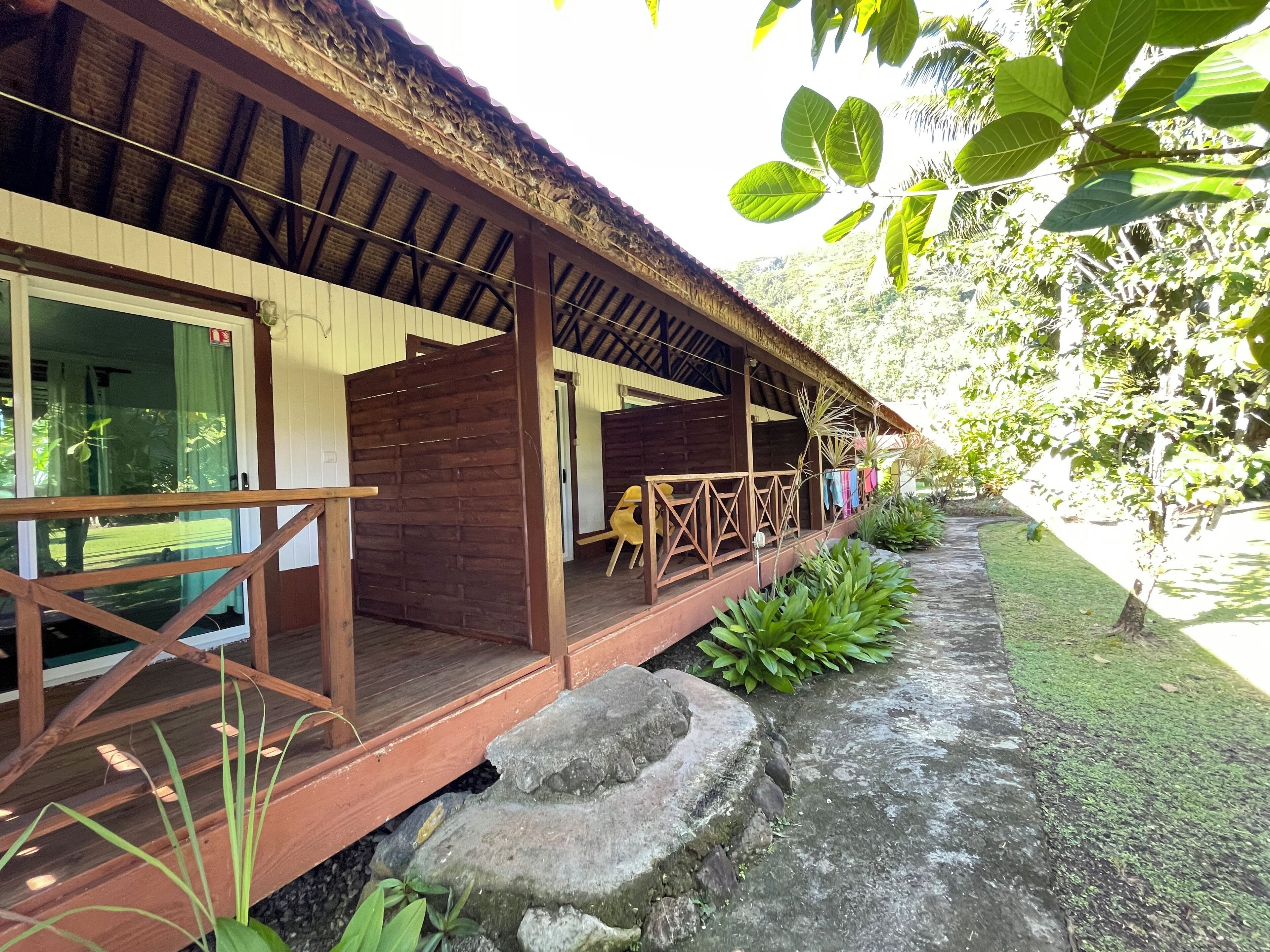 A wooden building with a covered porch, a stone pathway, and lush greenery.