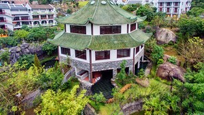 A traditional multi-story building with a green roof, surrounded by lush greenery and rocky terrain. - Nui Than Tai Ebisu Onsen Resort (Da Nang)