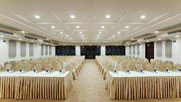 A conference room with rows of tables and chairs, a carpeted floor, and a high ceiling with recessed lighting.