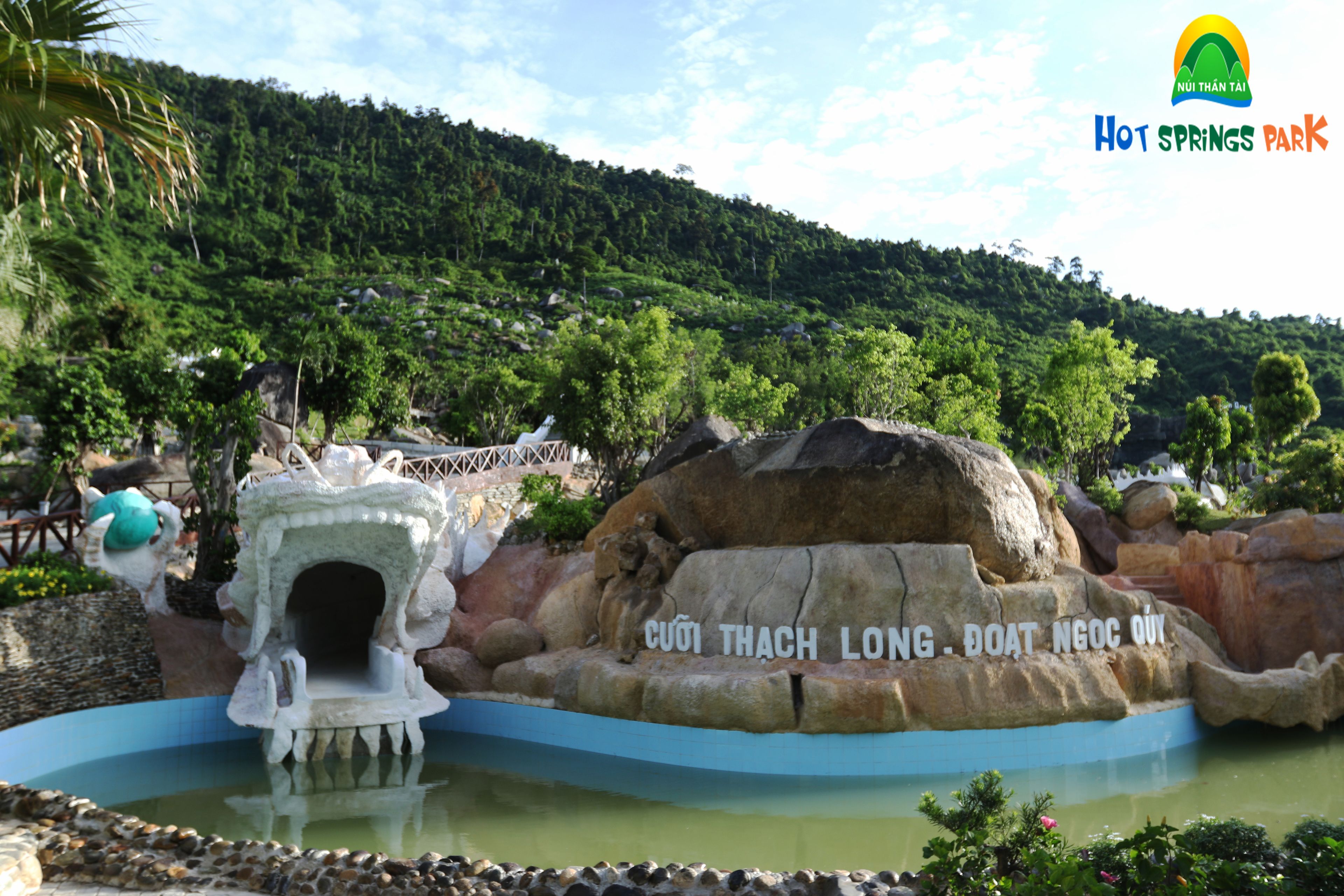 A water feature with a stone structure and a pool, surrounded by greenery and rocks.