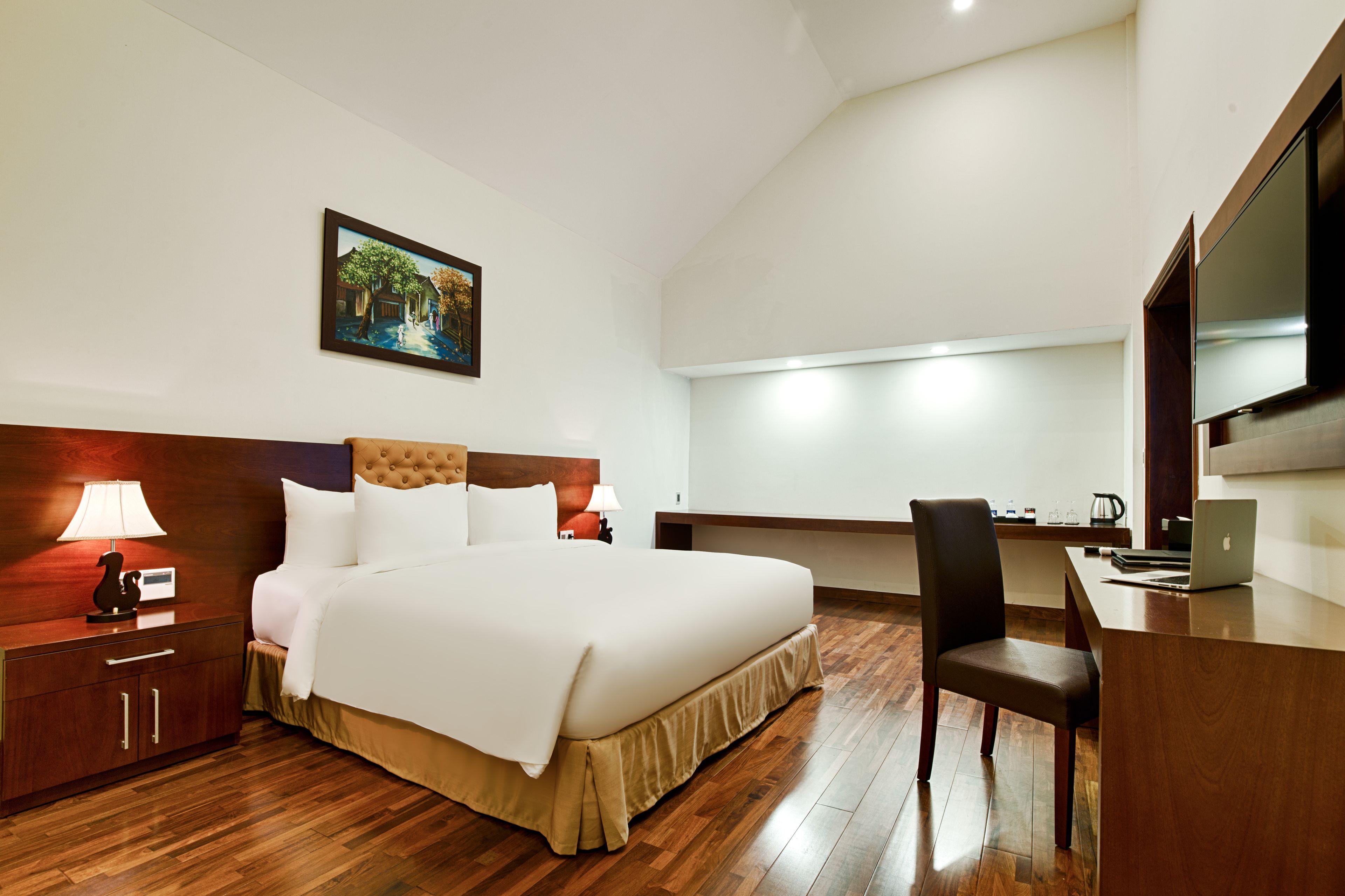 A hotel room with a bed, bedside table, lamp, desk, chair, and a TV.