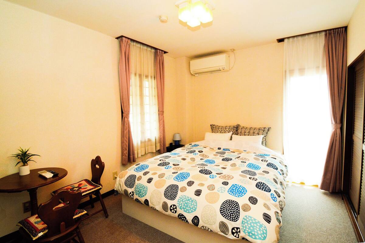 A hotel room with a bed, a small table with a plant, and a chair.
