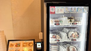 A vending machine with a menu and a digital display, a refrigerator stocked with food items, and a signboard with food options. - Belle Vue Nishiura (Minamiuonuma)