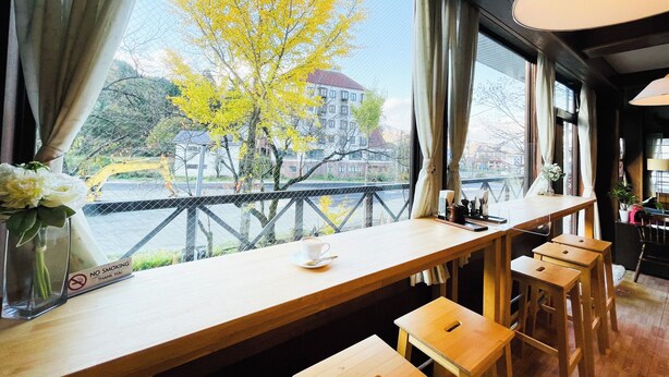 A café with a view of a river and buildings, wooden furniture, and a 'No Smoking' sign. - Belle Vue Nishiura (Minamiuonuma)