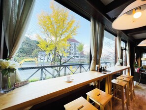 A café with a view of a river and buildings, wooden furniture, and a 'No Smoking' sign. - Belle Vue Nishiura (Minamiuonuma)