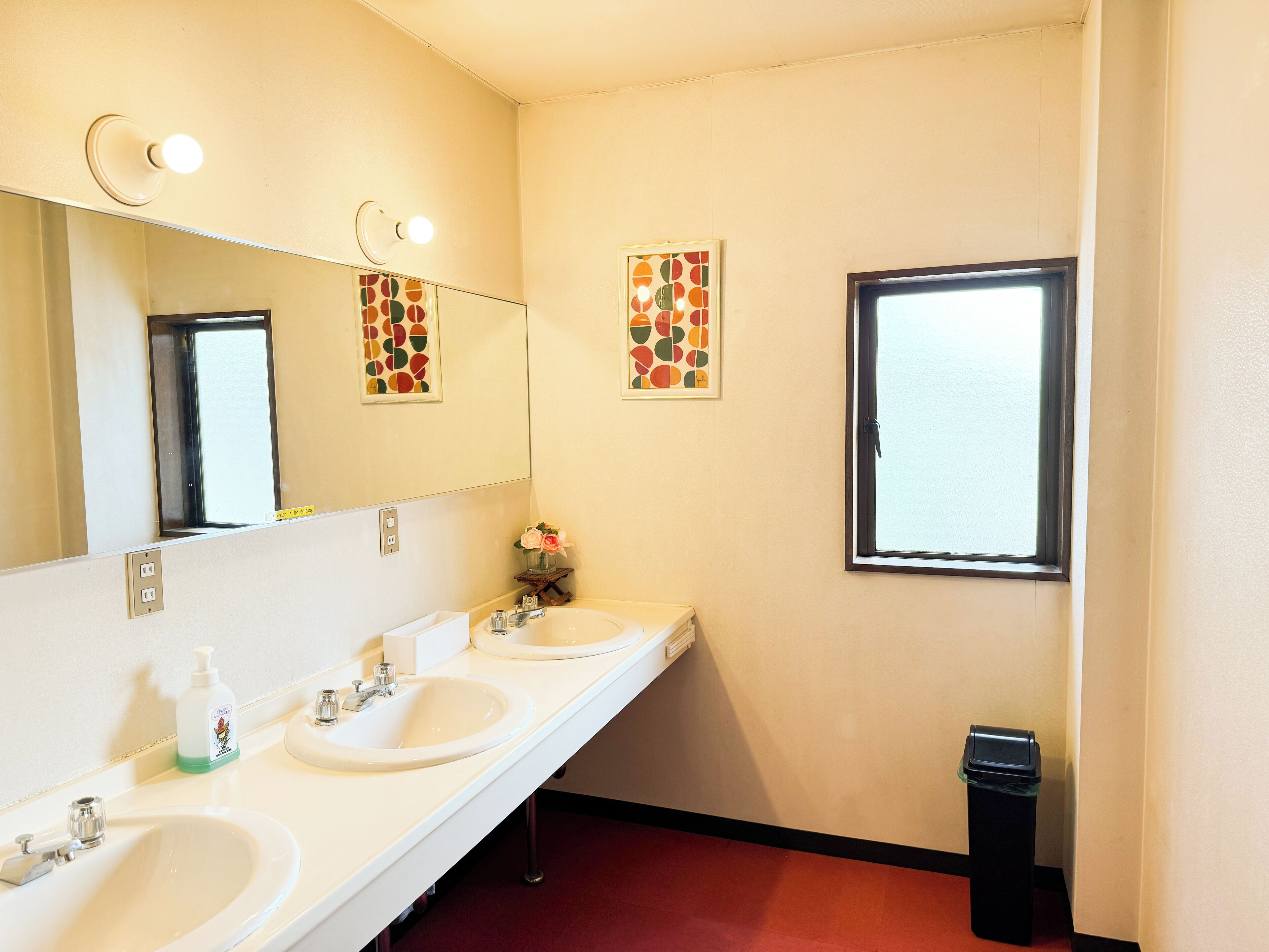 A bathroom with two sinks, a mirror, a window, and a trash bin.