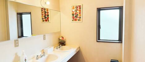 A bathroom with two sinks, a mirror, a window, and a trash bin.